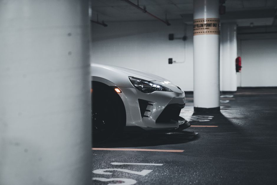 A sleek white sports car partially visible, parked in a dimly lit urban underground garage.